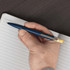 A blue recycled aluminium pen with a bamboo clicker is held above a lined notepad. The pen has a silver clip.