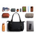 A black tote bag surrounded by various accessories including a drink bottle, pouches, a notebook, and a phone.