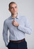 A slim fit long sleeve shirt in light blue with a subtle pattern, worn by a man adjusting the collar. The shirt has a logo.