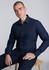A slim fit long sleeve shirt in navy blue, worn by a man seated on a wooden chair, featuring a branding logo.