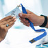 A blue lanyard with a badge holder is being exchanged between two hands. The lanyard is branded with the word "FITNESS."