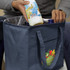 A drink bottle is being placed into a navy cooler bag with an interior lining, featuring a logo.