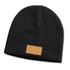 A dark grey cable knit beanie featuring a patch on the front. The beanie has a ribbed texture.