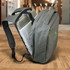 A grey anti-theft backpack with compartments, including space for a laptop, set against an indoor shopping backdrop.