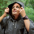 A woman wearing a grey rain poncho with a hood, looking upwards in a natural setting.