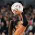 A netball being held above a player's head, featuring a distinctive design. The player has long dark hair and a sleeve on one arm.