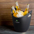 A black ice bucket filled with ice and three bottles of beer. It features a logo.