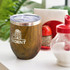 A drink bottle with a wooden finish and a silver lid, featuring a logo. Set against a background of condiments and greenery.