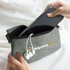 A grey tech pouch with a phone and white earbuds being placed inside. The pouch features branding.
