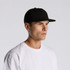A black cotton cap with a structured design, worn by a male model in a white T-shirt.