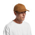 A brown cap with a curved brim and adjustable strap, featuring a logo on the side, worn by a model.