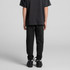 Black youth track pants are worn with a matching dark shirt and black shoes, showcased from the back.
