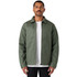 A man wearing a green service jacket over a white t-shirt, standing with a neutral expression. The jacket has a logo.