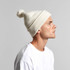 A white Pom Pom Beanie displayed on a model, featuring a fluffy pom pom on top and ribbed detailing.