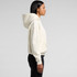 A cream-coloured hoodie with a hood, featuring a loose fit and a front pocket. It has a logo on the garment.