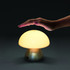 A mushroom-shaped table lamp with a white dome and a metallic base, with a hand positioned above it.