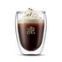 A double wall glass with a beverage topped with whipped cream and chocolate shavings, featuring a logo.