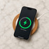 A wireless charger with a cork base and a smartphone displaying a green charging icon on a marble surface.