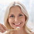 A bamboo toothbrush is held by a woman smiling, with a small amount of toothpaste on the bristles.