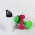 A drink bottle in white with a black flip straw lid, next to green and pink dumbbells against a speckled background.