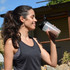 A drink bottle with a black lid and a clear body, held by a person outdoors, featuring a logo.
