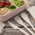 A cutlery set in a light cream colour, featuring a knife, fork, and spoon, alongside a pastel pink lunchbox with food.