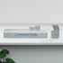 A white weekly pill box with multiple compartments, some open, alongside white pills and a plant. It has a logo.