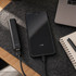 A black 5,000mAh power bank connected to a smartphone on a desk with a laptop and notebook.