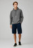 A man wearing a grey hoodie and navy shorts stands casually. The shorts feature pockets and a logo.