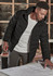 A black unisex puffer jacket with a hood, worn by a person examining blueprints indoors. The jacket has a logo.