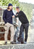 Two men wearing work pants in beige and black, standing beside a vehicle in a forested area. Both have casual attire and a logo on the clothing.
