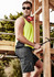 A man wearing a vibrant yellow athletic tank top and dark grey board shorts, with sunglasses and headphones, poses with a hammer.