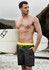 Men's streetwear board shorts in dark grey with a bright yellow drawstring, paired with a surfboard.