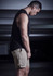 A man wearing khaki sports shorts and a black sleeveless top, standing in a dimly lit space.