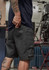 Men's rugged shorts in dark grey with utility pockets, featuring a logo on the side and a fitted design.