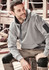 A grey unisex multi-pocket hoodie featuring a logo, worn by a person sitting on a wooden surface.
