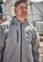 A light grey unisex packable rain jacket features a front pocket and a hooded design. The model is wearing it outdoors.