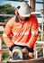 A person wearing an orange long sleeve polo shirt with segmented reflective tape operates a circular saw, wearing a helmet and ear protection.