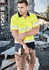 A unisex hi-vis segmented tape short sleeve polo in bright yellow and navy, featuring reflective stripes, held by a man on a worksite.