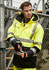 A men's waterproof jacket in bright yellow and black, featuring reflective stripes and a logo, worn by a man.