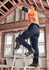 A man in orange and grey high-visibility workwear wears navy cargo pants while standing on a ladder.