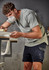 A man wearing a grey t-shirt and navy shorts, working on a project with a mask on in an indoor workspace.