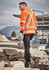 A man wearing an orange high-visibility jumper with reflective stripes, holding a hammer, in a construction setting.