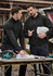 Two men in black, unisex merino wool mid-layer pullovers are discussing plans at a construction site.