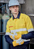 A man in a yellow and navy work shirt with reflective stripes, wearing protective goggles and gloves, standing near gas cylinders.