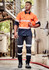 A worker in an orange and navy long sleeve shirt with segmented tape, holding a helmet in an industrial setting.