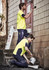 A bright yellow men's high visibility T-shirt worn by two men painting a wall, one standing and one kneeling.