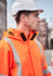 An orange heavy-duty waterproof jacket with reflective strips, worn by a person in a hard hat.