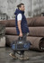 A man wearing a navy hooded puffer vest holds a black and navy duffle bag, standing against industrial backdrops.