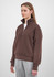 A brown women's 1/4 zip jumper is displayed on a model, paired with grey pants and featuring a branded logo.
